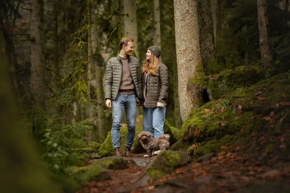 Mann und Frau stehen sich im Wald gegenüber zu ihren Füßen steht ihr kleiner Hund