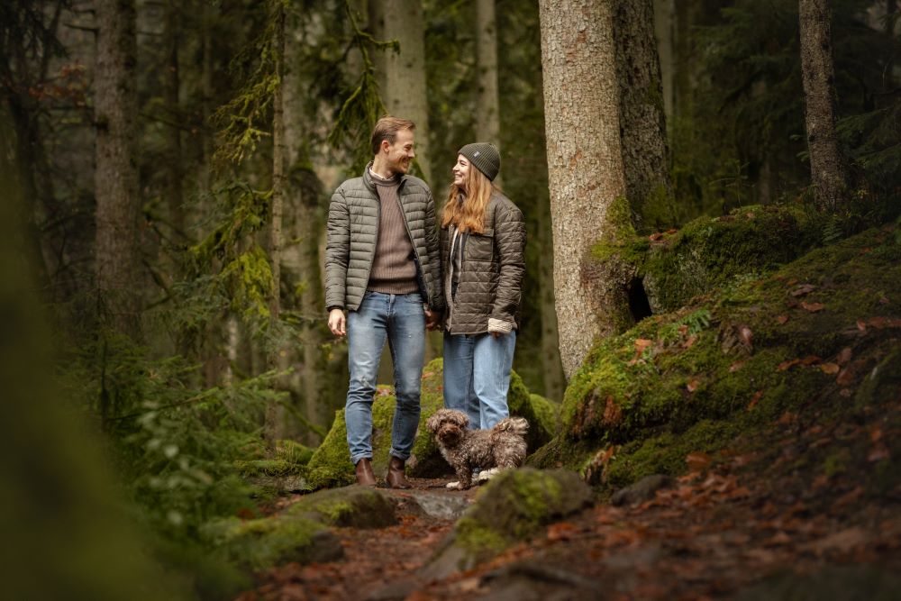 Mann und Frau stehen sich im Wald gegenüber zu ihren Füßen steht ihr kleiner Hund