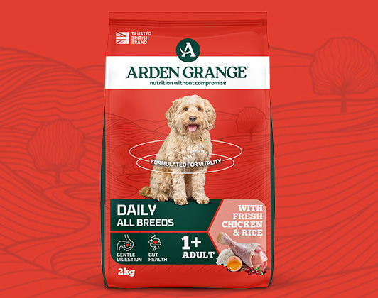 Bag of Arden Grange Adult dog food with fresh chicken and rice against a red background. The packaging features a happy dog image and text reading “Wholesome maintenance diet – Naturally hypoallergenic – Made in the UK.”
