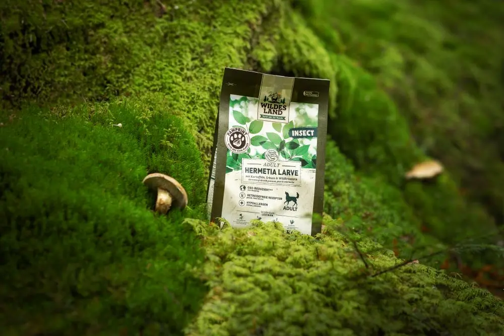 Eine 1kg Packung Insect PawPrint steht auf einem mossigen Waldbodem umgeben von zwei großen Pilzen.
