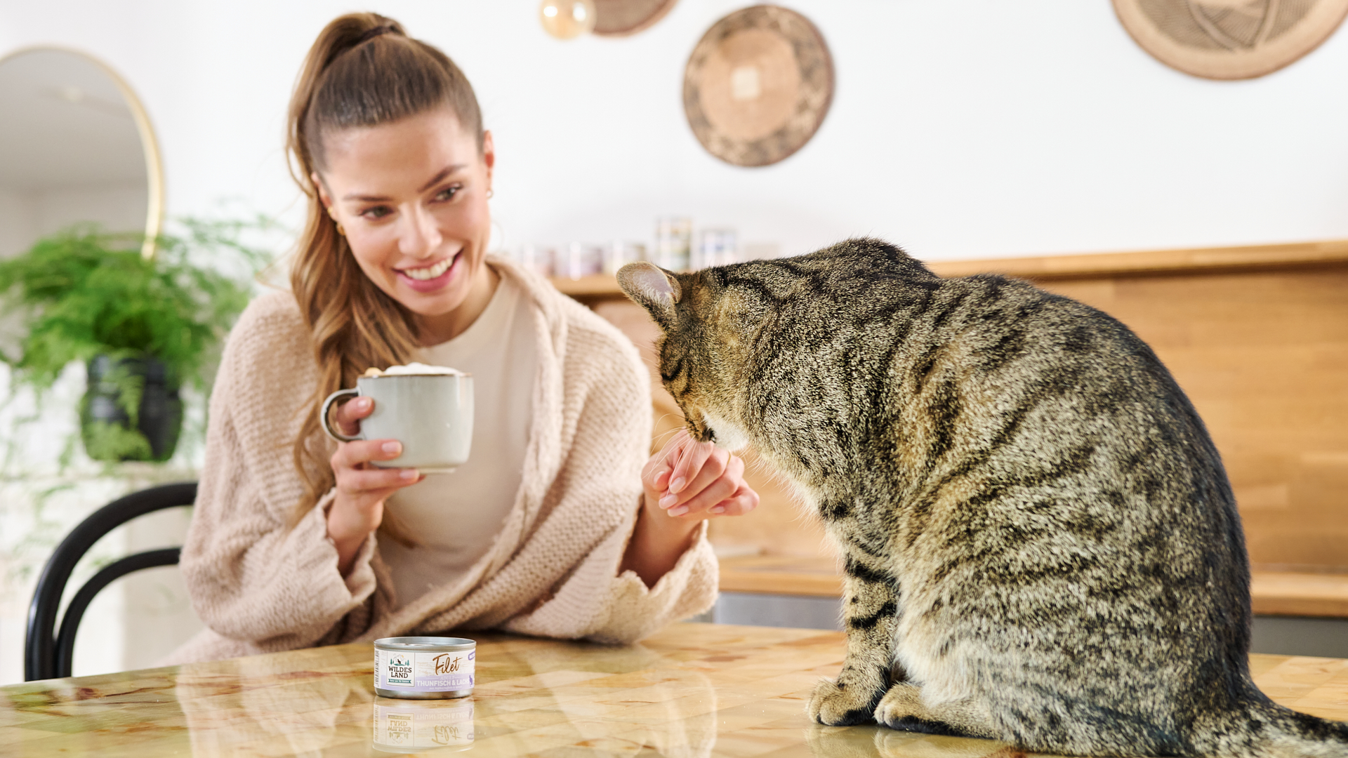 Katze sitzt neben ihrem Frauchen auf dem Tisch, daneben steht eine Dose Nassfutter Filet von Wildes Land.
