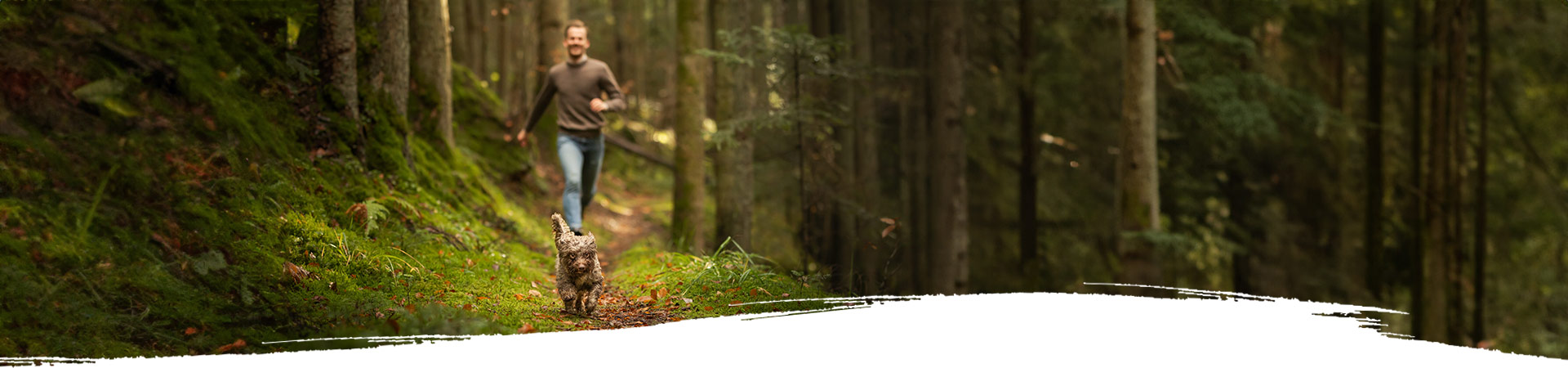 Mann rennt fröhlich mit seinem kleinen Hund durch den Wald