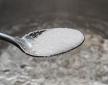 A close-up of a metal spoon holding salt above a blurred background.
