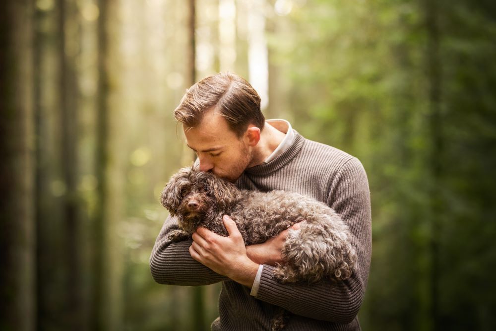 Ein Mann hat seinen kleinen Hund auf dem Arm und küsst ihn auf den Kopf